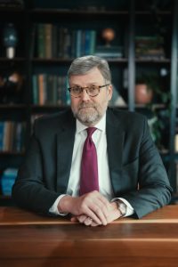 Portrait of BOV member Chris Tuttle sat at a desk in front of a bookshelf.